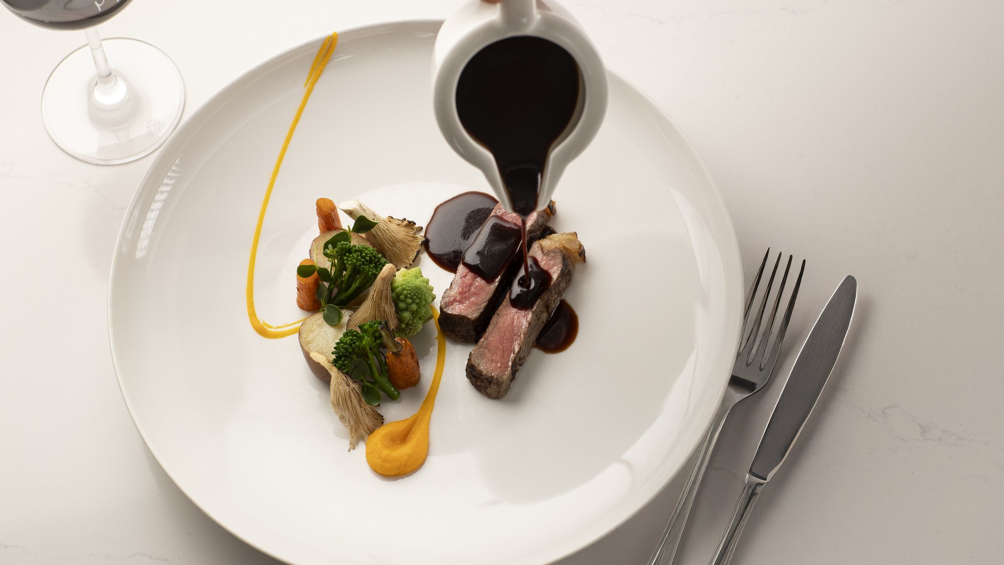 Een biefstuk die wordt overgoten met jus en een glas rode wijn