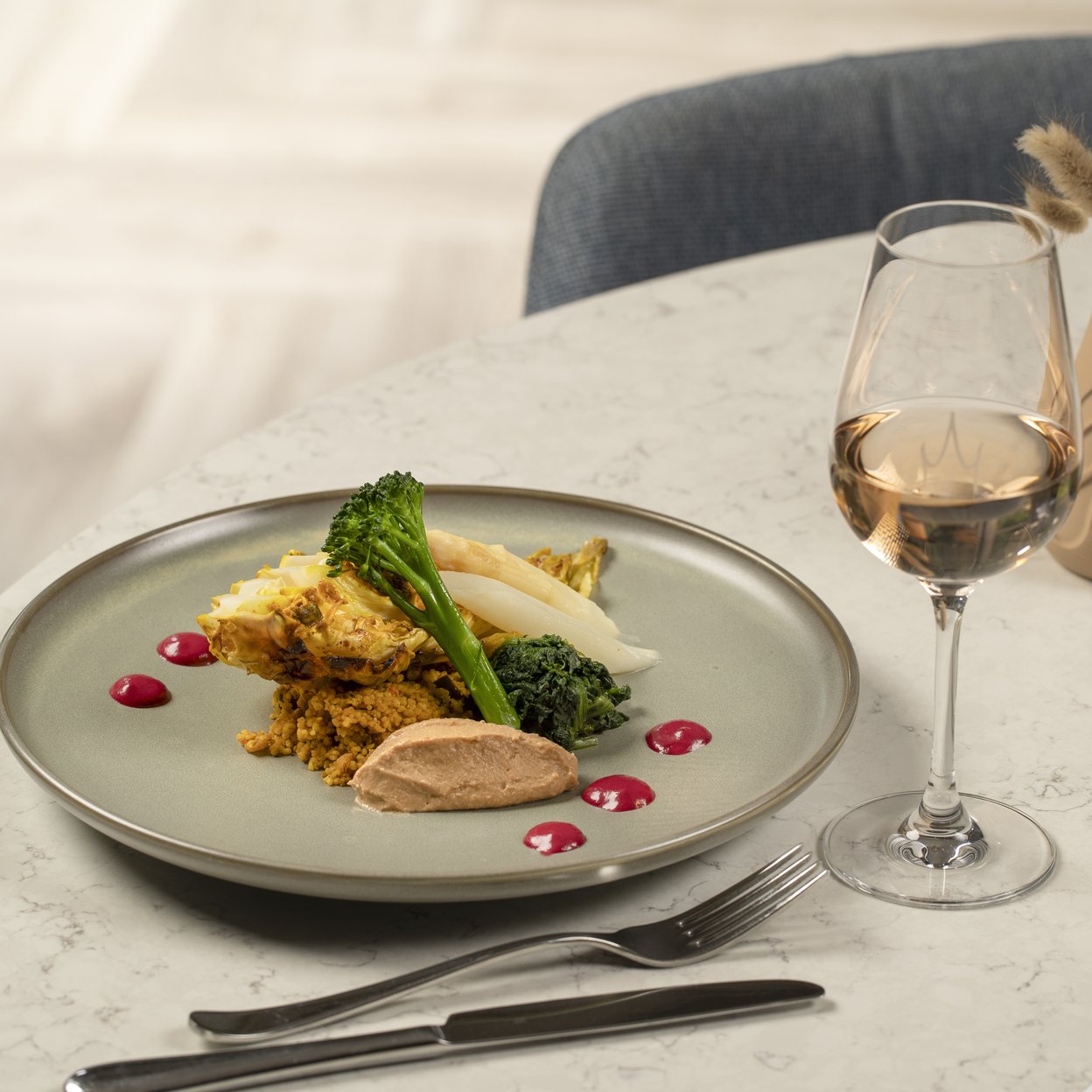 Verfijnd restaurant gerecht met quinoa, groene groenten en asperges, geserveerd met witte wijn op marmeren tafel.