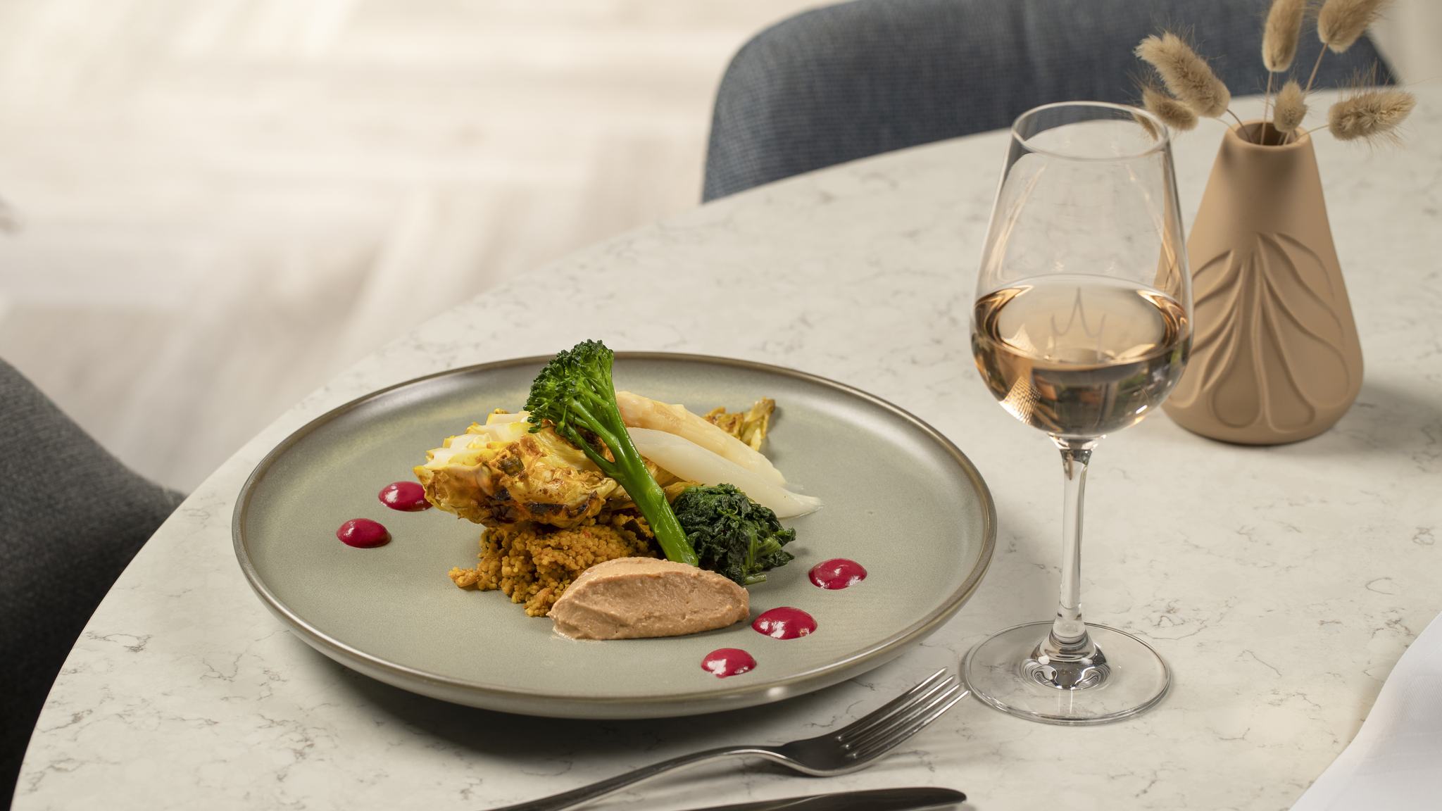 Verfijnd restaurant gerecht met quinoa, groene groenten en asperges, geserveerd met witte wijn op marmeren tafel.