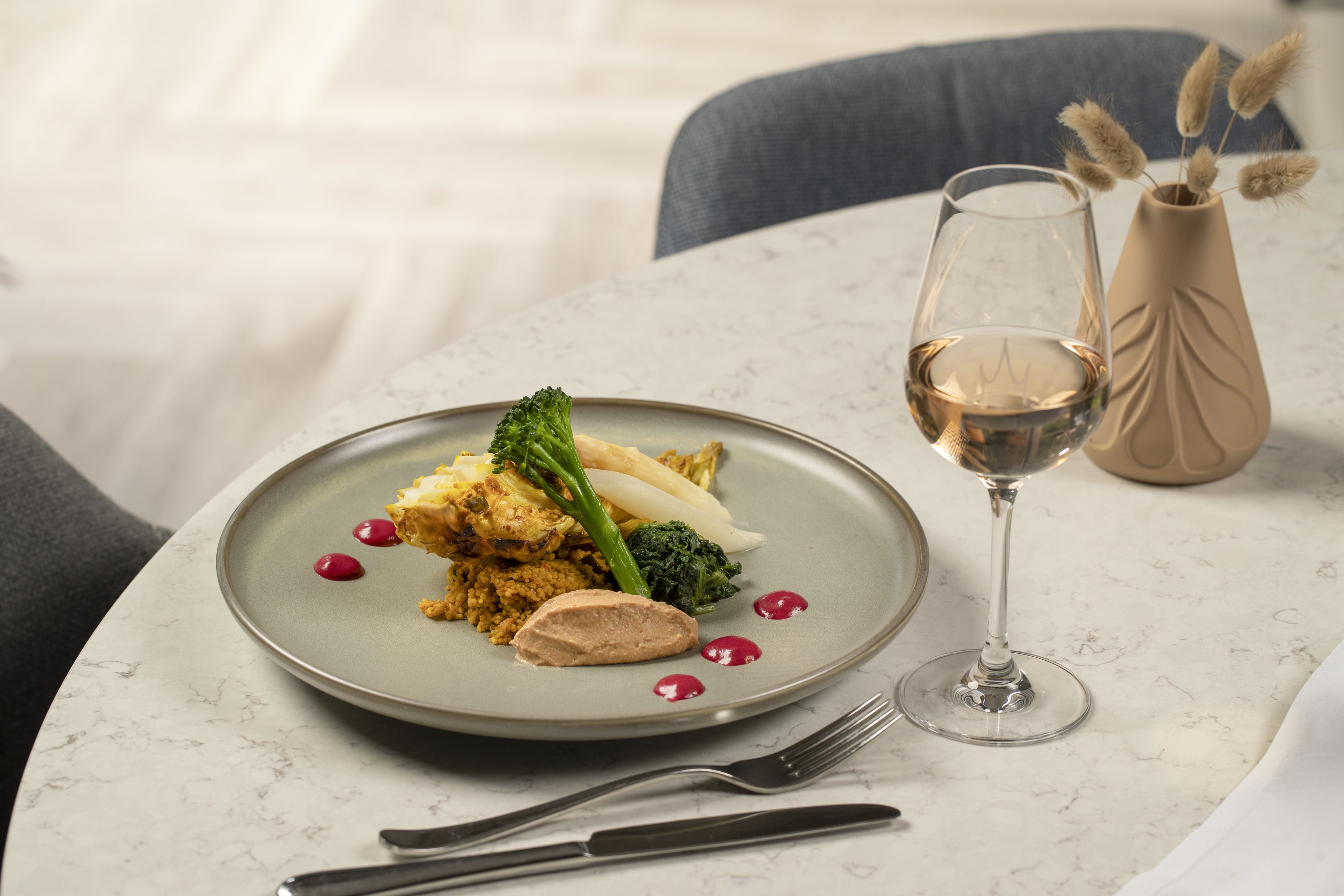 Raffiniertes Restaurant-Gericht mit Quinoa, grünem Gemüse und Spargel, serviert mit Weißwein auf Marmortisch.