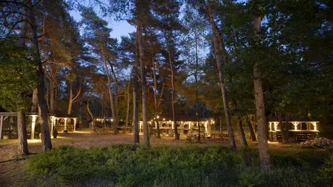 Sfeervolle avondverlichting op de buitenplaats bij Residence Heideborgh met verlichte paviljoens en picknicktafels tussen de bomen.