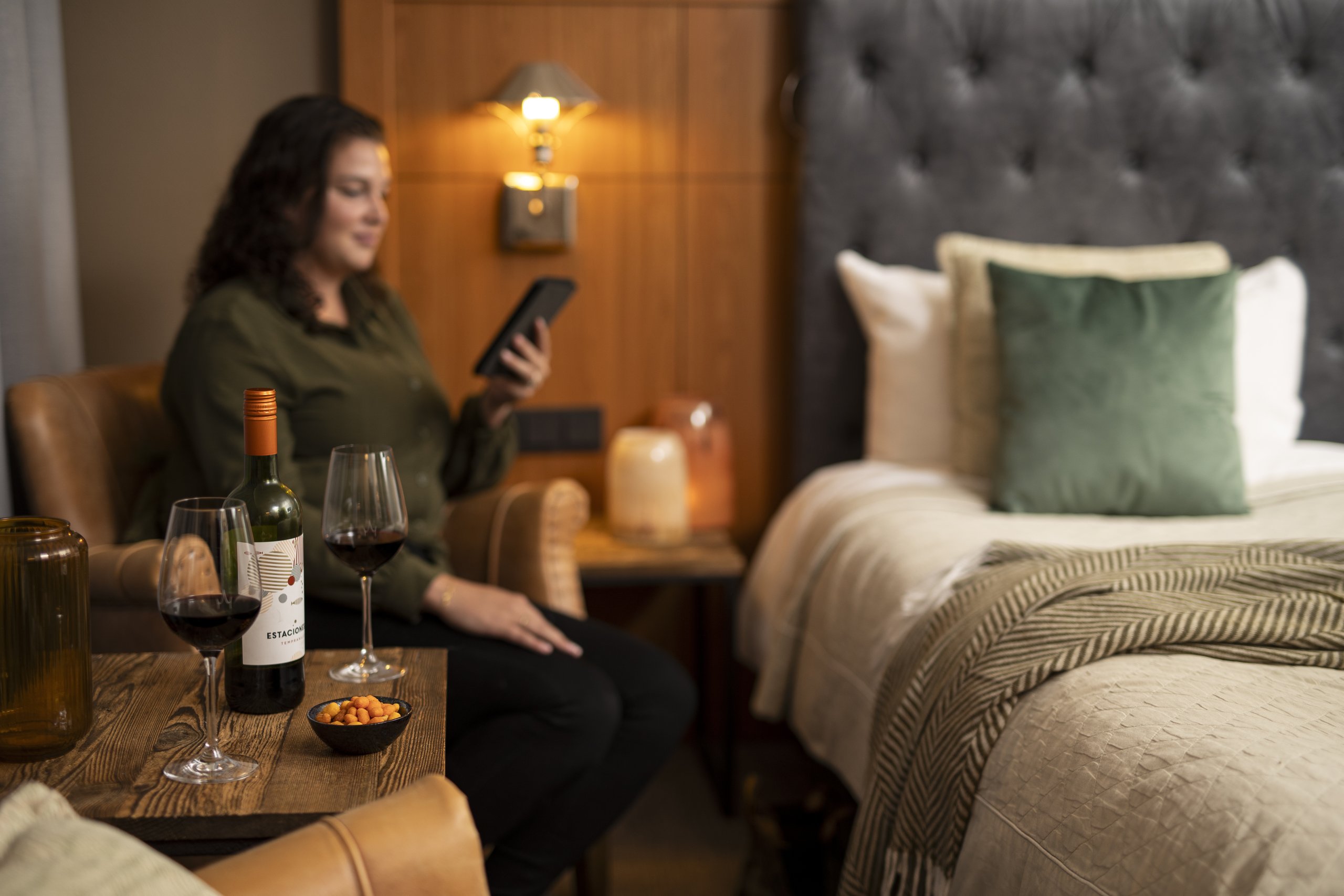 A woman in a hotel room with her e-reader and red wine.