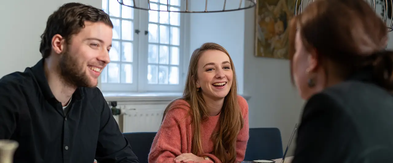 Drie lachende mensen aan de vergadertafel