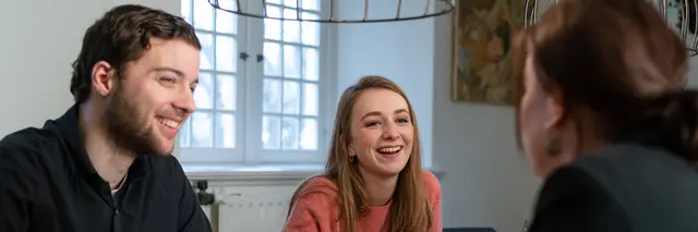 Drie lachende mensen aan de vergadertafel