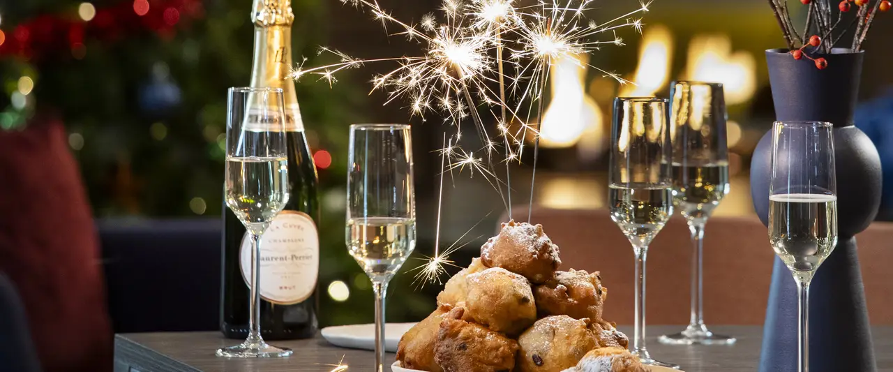 Een gedekte tafel met champagne en oliebollen.