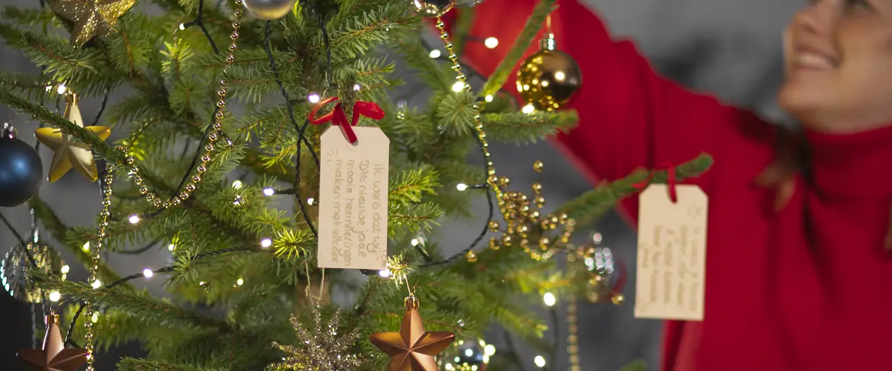 Een vrouw die vrolijk de kerstboom optuigt.