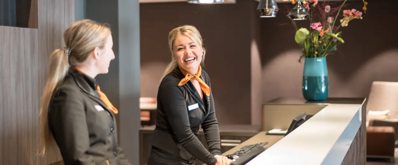 Twee lachende receptionistes aan de receptiebalie van het hotel